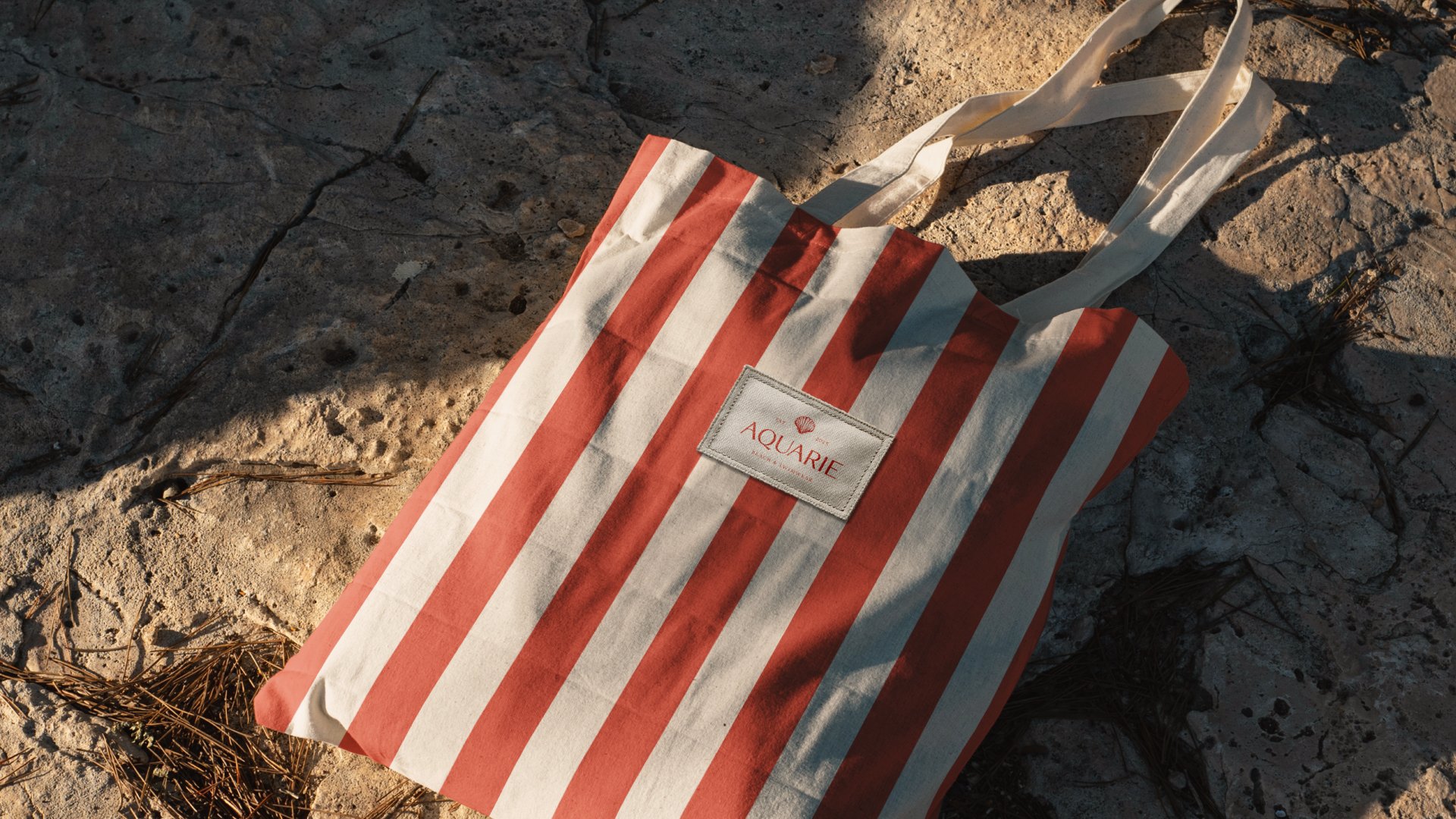 Ecobag Aquarie com listras vermelho coral e creme sobre pedra ao sol